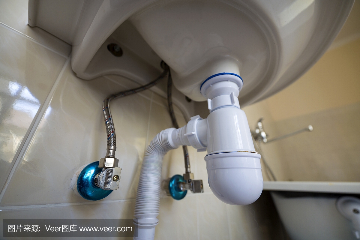 在浴室浅米色瓷砖的背景上,新的白色洗手盆水槽连接到下水道的底部视图。专业的管道安装理念。